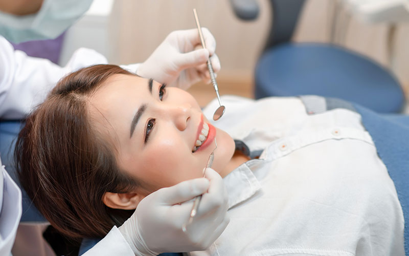 Dental patient receiving treatment with a smiling expression, assisted by dental professionals in a clinical setting.