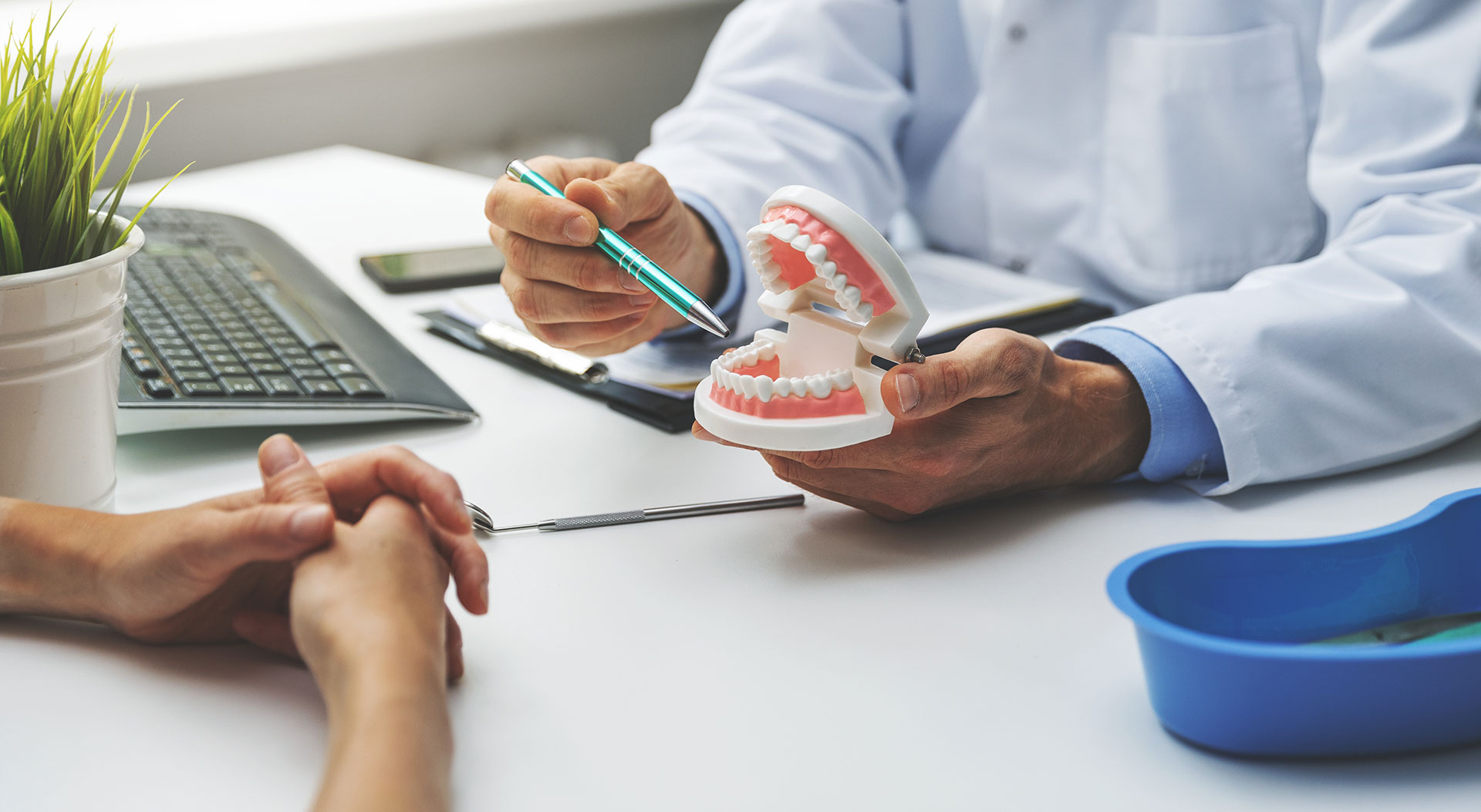 A dental professional is assisting a patient with a tooth model, demonstrating the process of fitting a dental implant in a clinical setting.