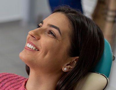 A woman is seated in a dental chair, smiling and looking upwards.