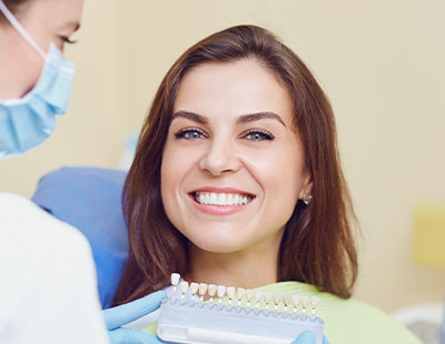 A dental professional is smiling at the camera while performing a dental procedure on a patient.